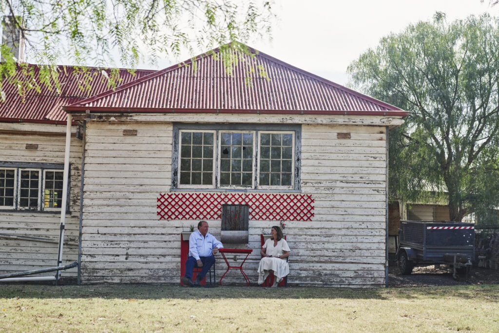 Bill and Sharon Green sitting on red chairs in front of old Exford heritage homestead